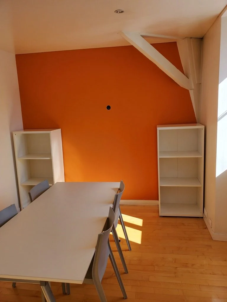 Salle de réunion partagée : table pour six à huit personnes devant un mur orange